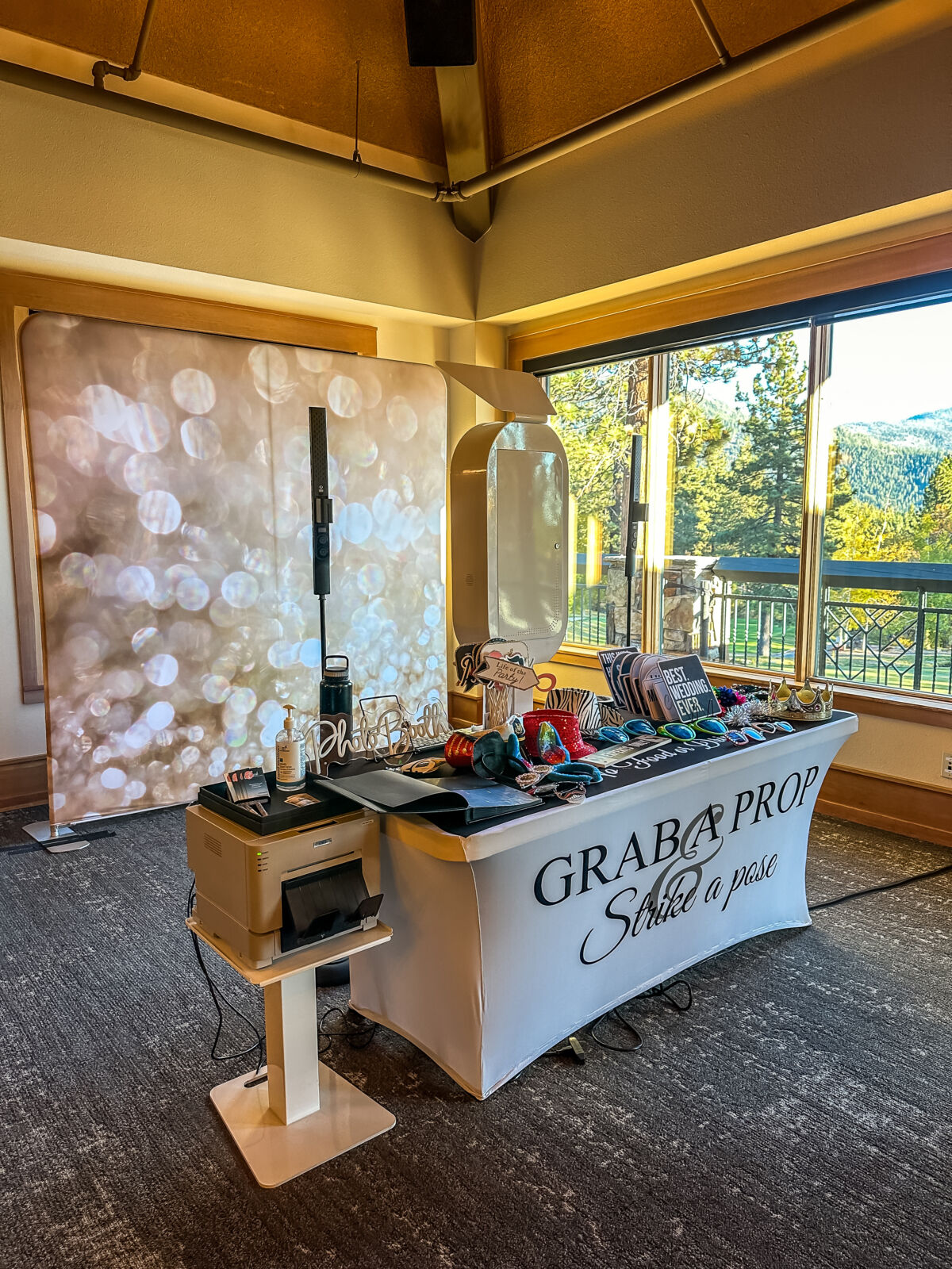 Full photo booth setup at a golf-club room with a bokeh backdrop and a "grab a prop" table banner