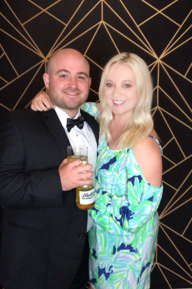 A couple in formal attire posing in the photo booth in front of a gold geometric backdrop