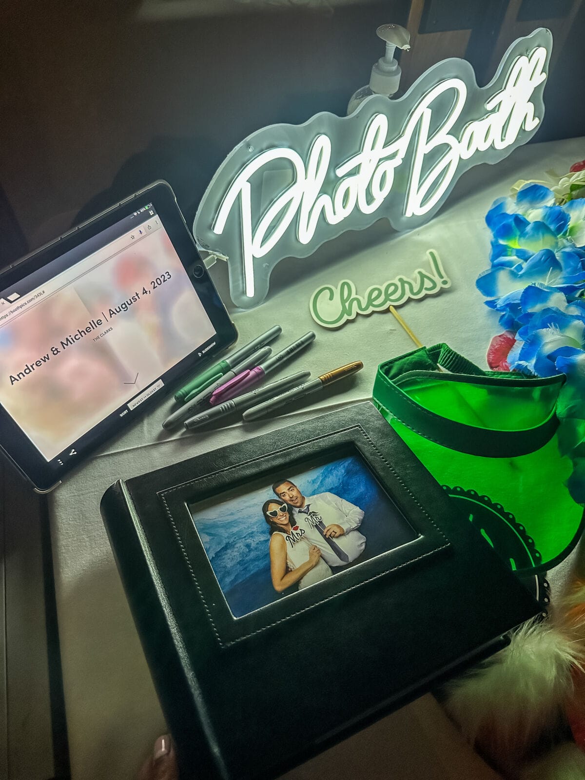 Photo Booth neon sign beside a tablet showing the online gallery and a keepsake print album