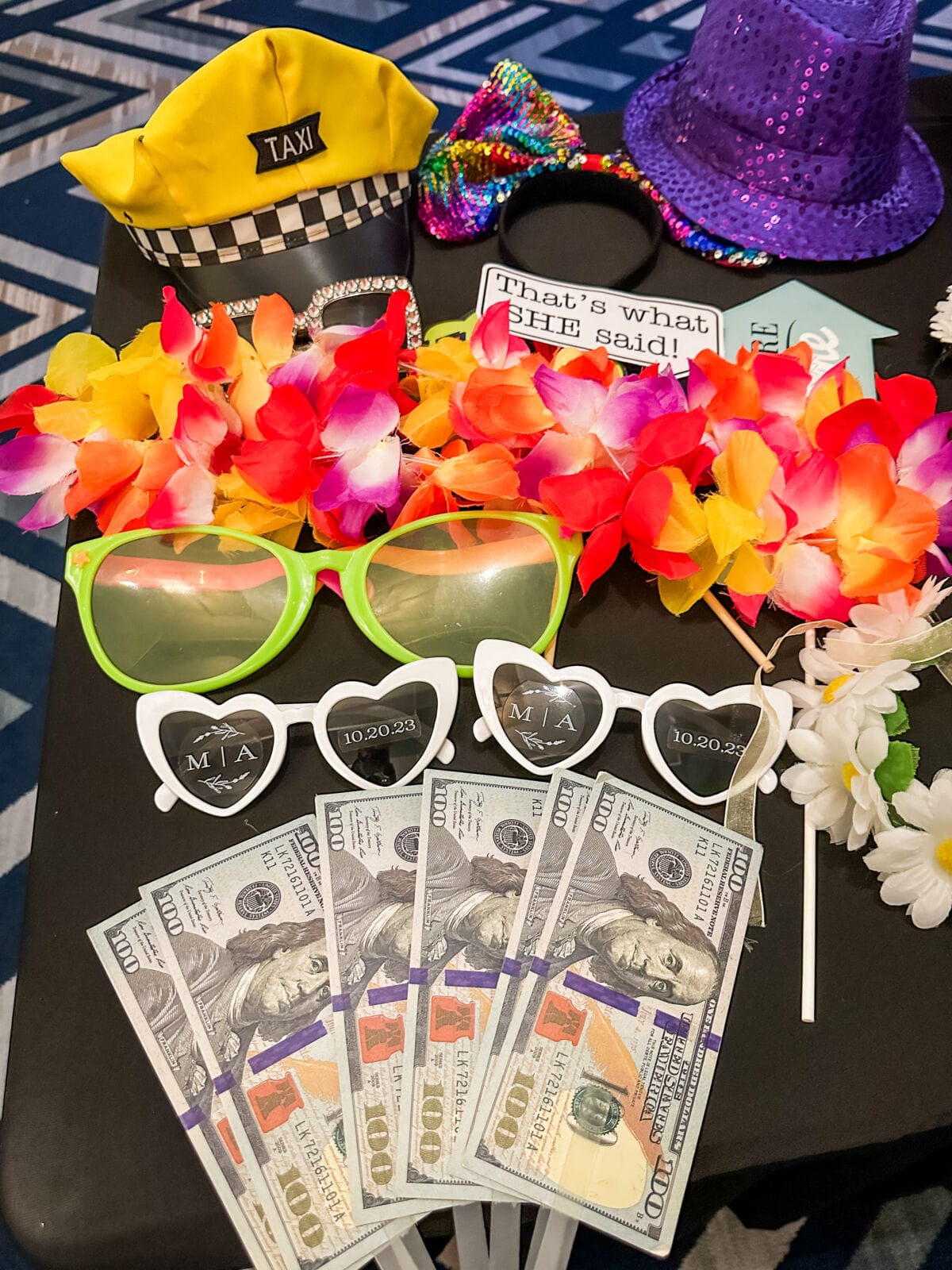 Flat lay of photo booth props including a taxi hat, sequin hat, leis, custom heart glasses, and play money