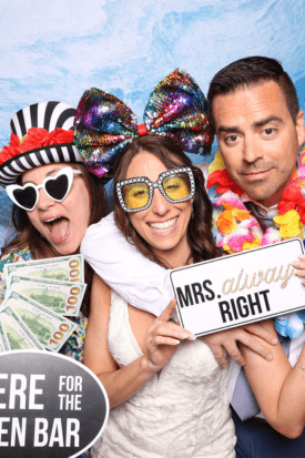 Three wedding guests posing with heart sunglasses, a lei, and a "Mrs. Always Right" sign in the photo booth