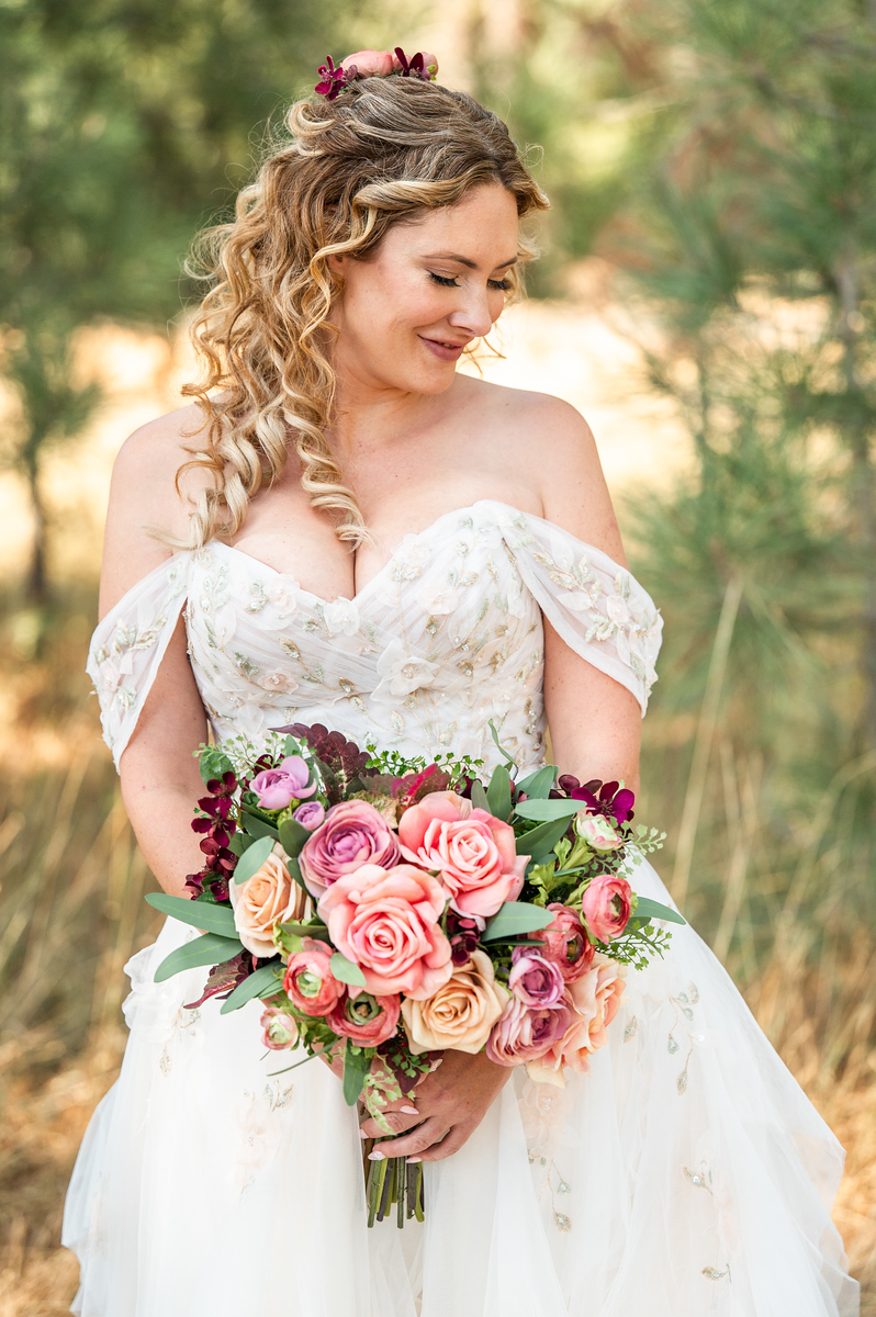 Bride in an off-the-shoulder gown looking down at her pink and burgundy bouquet