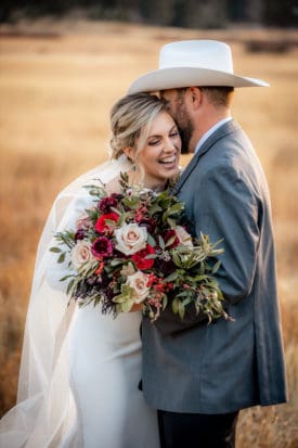 Bride laughing with her bouquet beside a groom in a white cowboy hat in a golden field