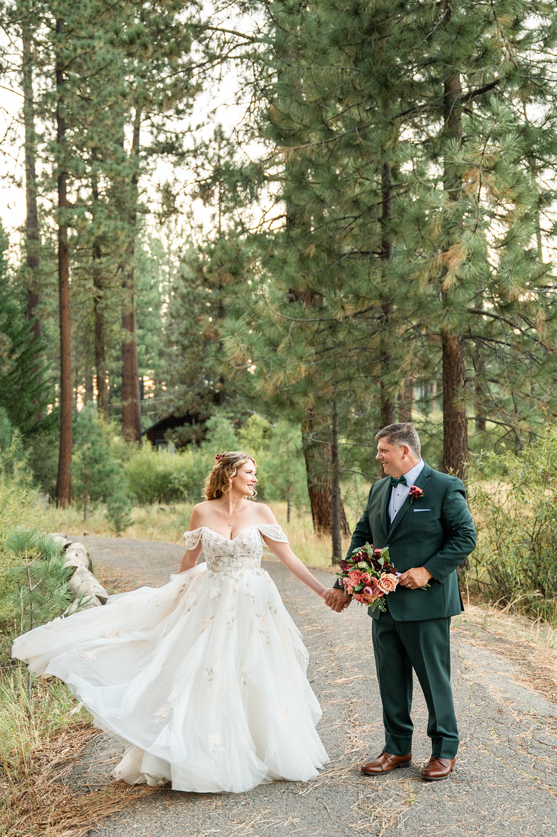 Couple holding hands on a pine-forest path, the groom in a green suit