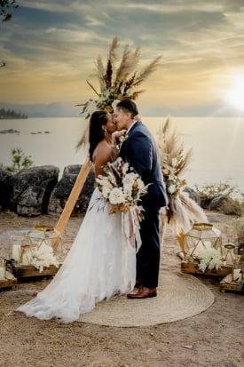 Couple kissing beneath a pampas-grass ceremony arch overlooking Lake Tahoe at sunset