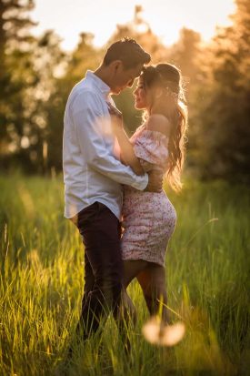 Engaged couple embracing forehead to forehead in a golden grass field at sunset