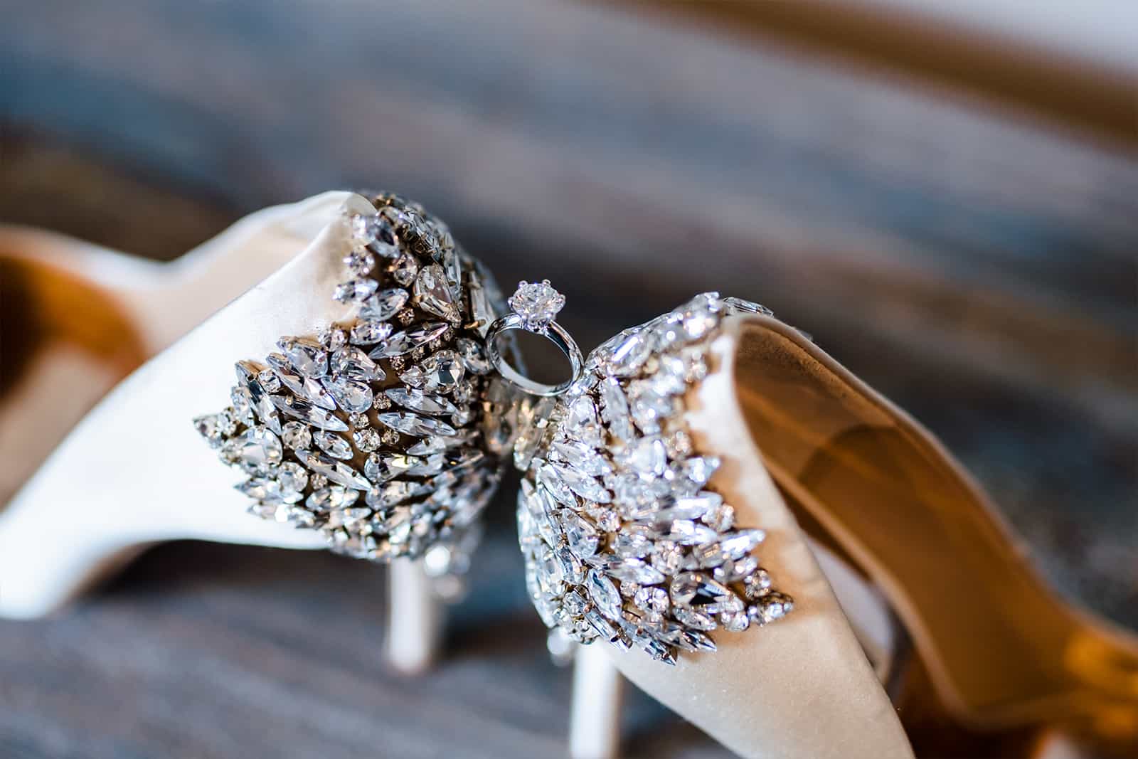 Macro detail of sparkly rhinestone bridal heels with an engagement ring balanced between them