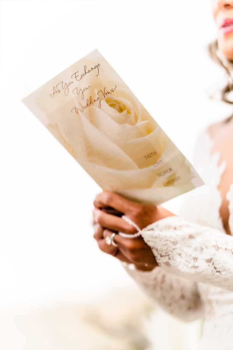 Bride’s hands holding an As You Exchange Your Wedding Vows program over a cream rose design