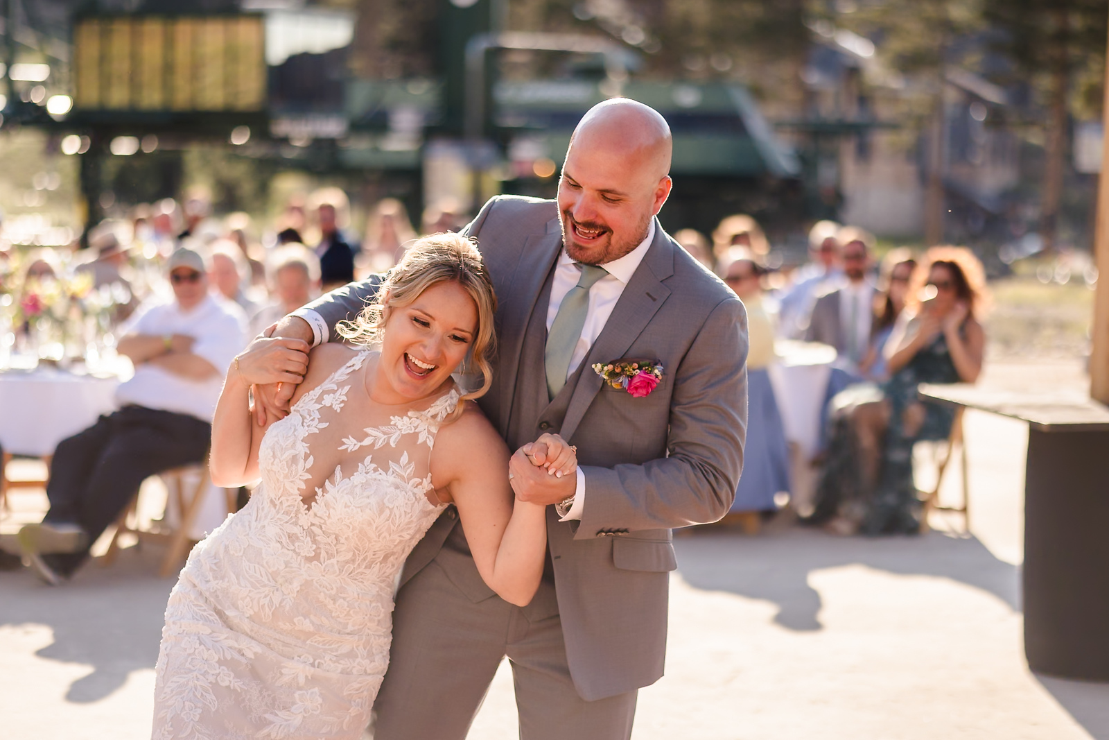 A laughing bride and groom sharing a joyful first dance at a sunny outdoor reception